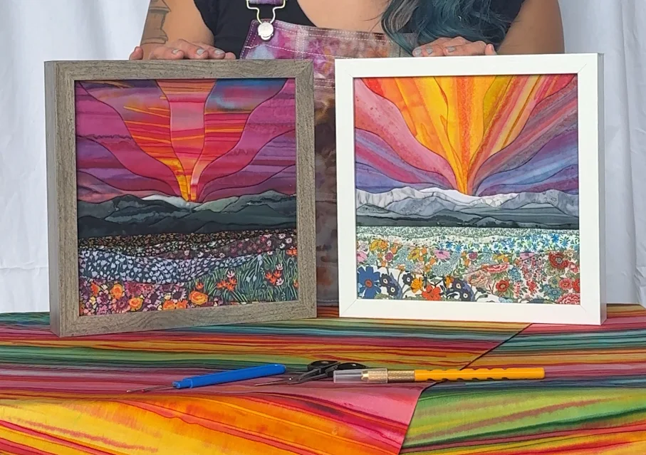 Two finished kinusaiga landscapes from the same template side by side: berry sunset batiks and golden sunrise batiks, with Hannah's tools in front